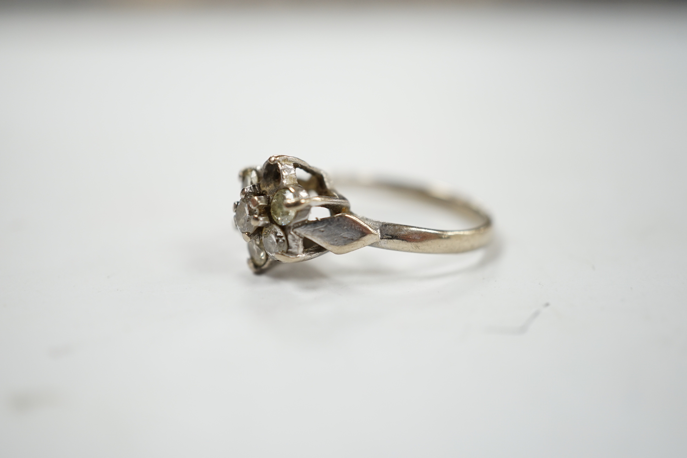 An 18ct white metal and seven stone diamond cluster set flower head ring (one stone missing), size K/L, gross weight 3.4 grams.